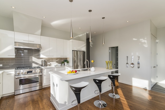 Bright modern renovated kitchen interior featuring clean white countertops, new light fixtures, and polished wooden flooring Bright modern renovated kitchen interior featuring clean white countertops, new light fixtures, and polished wooden flooring